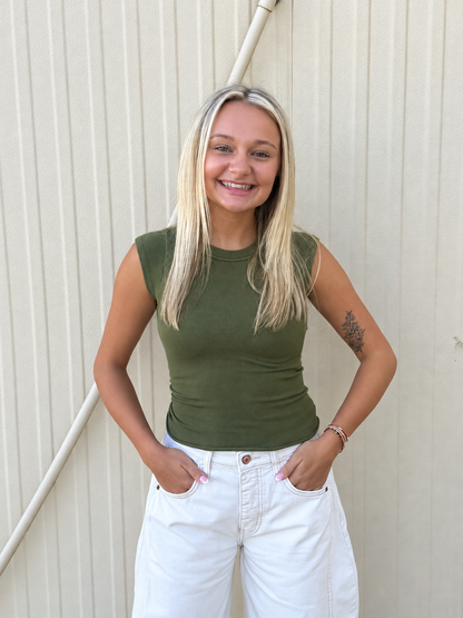 Model wearing the Free People So Soft Seamless Modal Baby Tee in Ferngully Olive, featuring a fitted ribbed design, crew neckline, cap sleeves, and waist-length silhouette, styled with white denim jeans for an effortless everyday look.