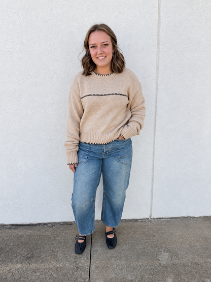 Model wearing Free People We The Free Minimalist Moxie Barrel Jeans in light-wash blue denim, featuring a relaxed fit, wide barrel-leg silhouette, ankle-length hem, and oversized back pockets, styled with a tan contrast stitch sweater and black Mary Jane flats.