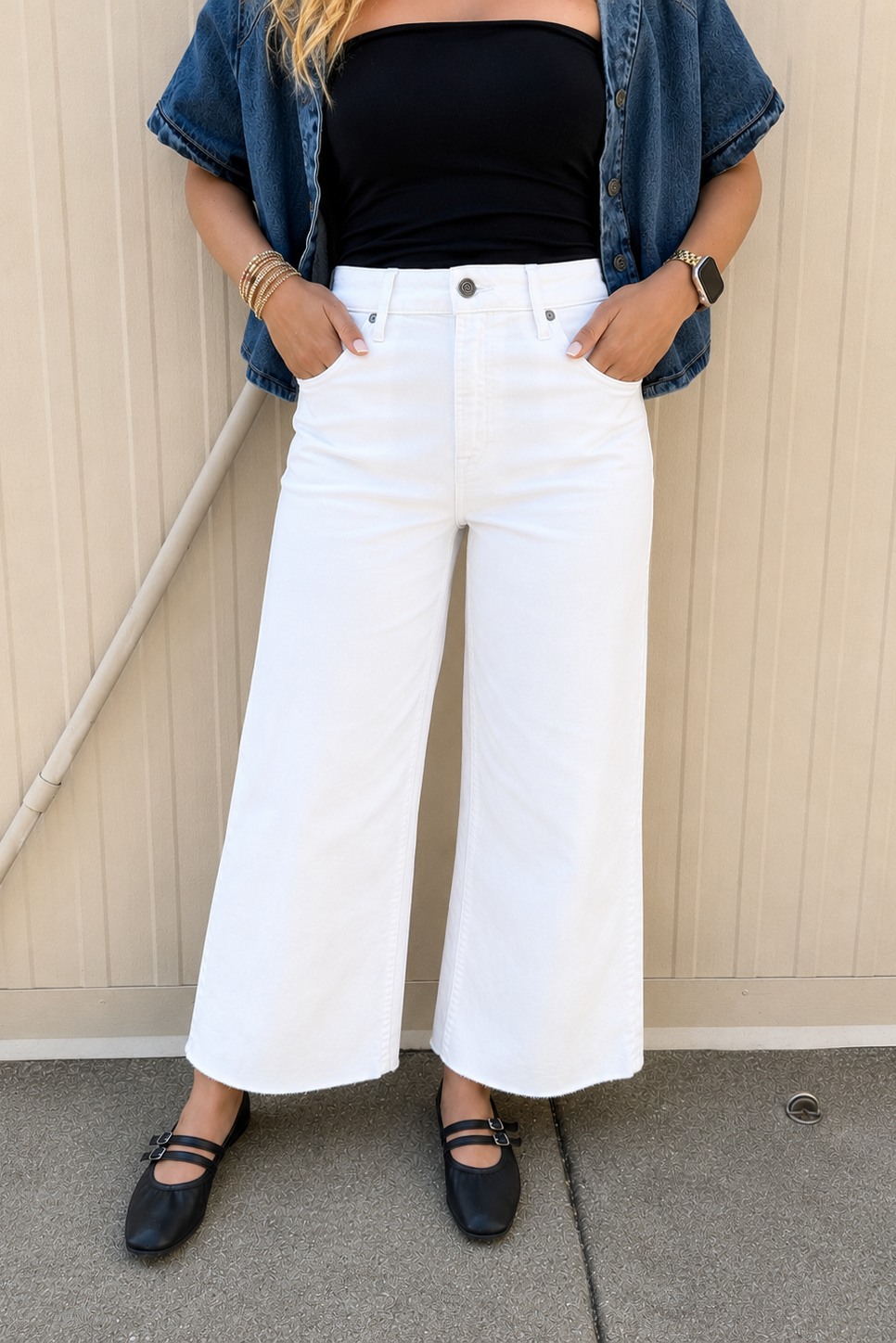 Women’s white cropped wide leg jeans styled with a black strapless tube top and medium wash cropped denim button-up shirt. Features a high-rise fit, clean white denim, cropped wide leg silhouette, raw hem, and side slit detail, paired with black Mary Jane flats for a casual summer outfit.