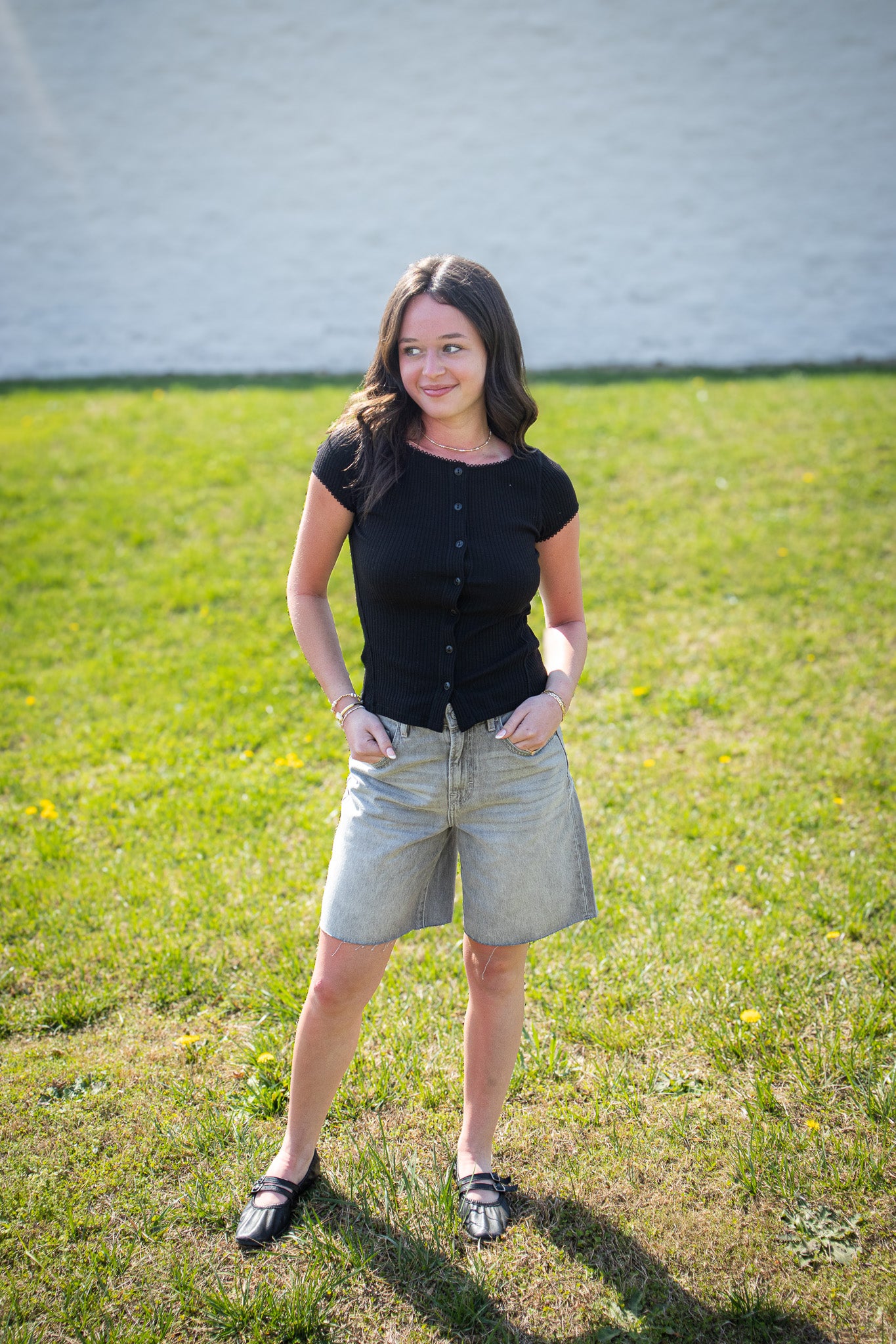 Person wearing a black shirt and light shorts standing on grass with a white wall in the background