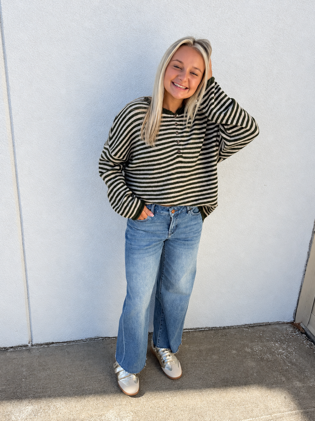 Model wearing Hidden Logan Medium Wash Mid Rise Petite Dad Jeans, featuring a relaxed straight-leg fit, light fading, and full-length denim silhouette, styled with an olive green and cream striped henley sweater and metallic sneakers.