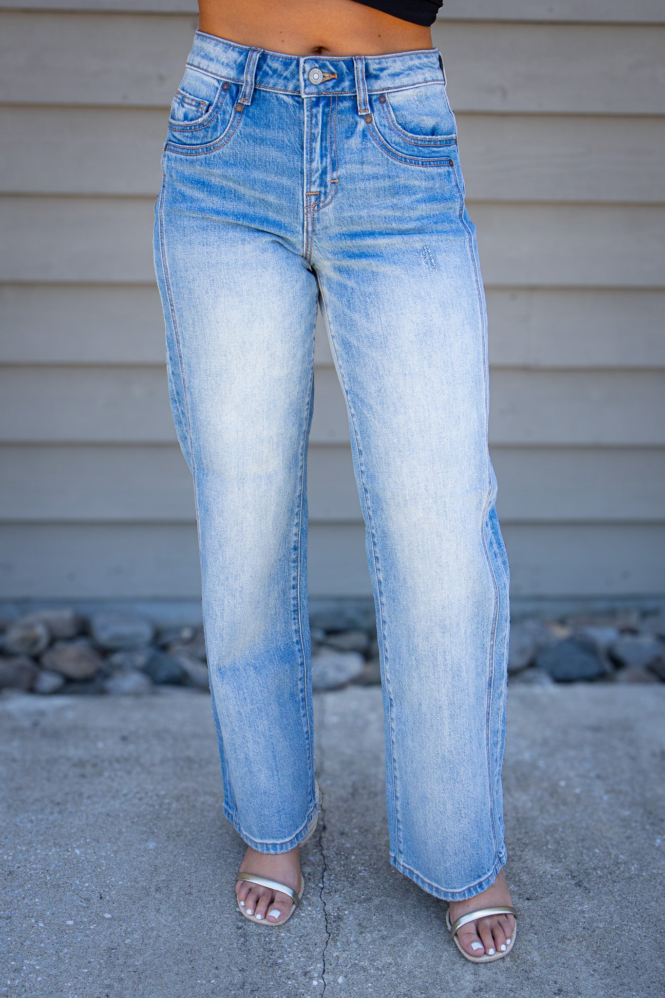 Women’s light wash high rise straight leg jeans with subtle distressing styled with black crop top and nude heels.
