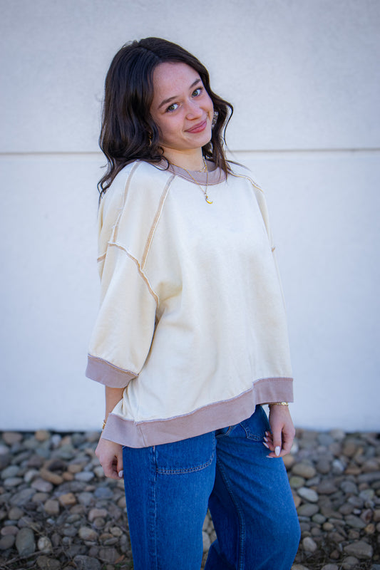 Woman wearing a light-colored sweater and blue jeans standing against a white wall.