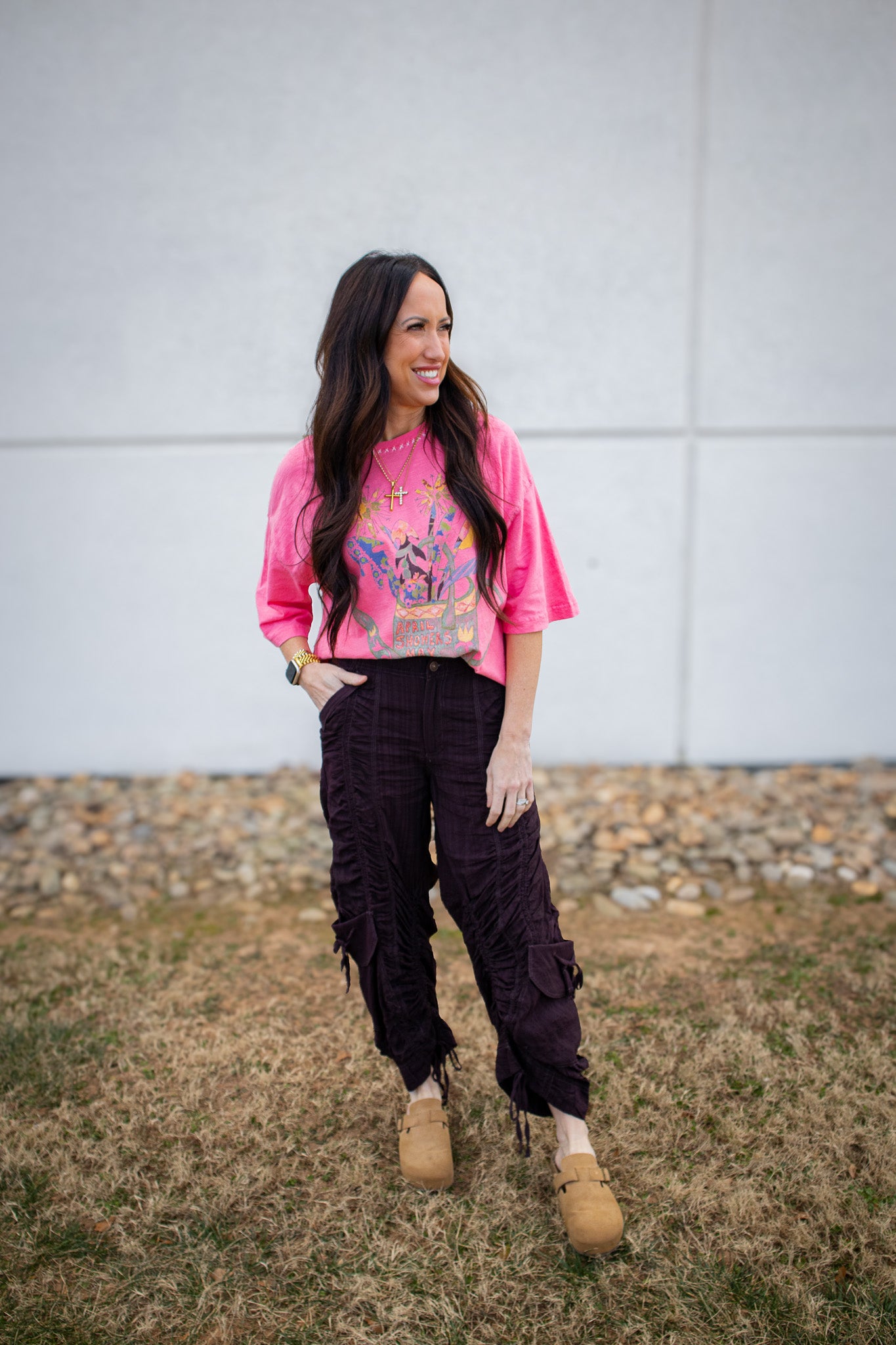 Woman wearing a bright pink shirt with a graphic design and dark pants standing outdoors.
