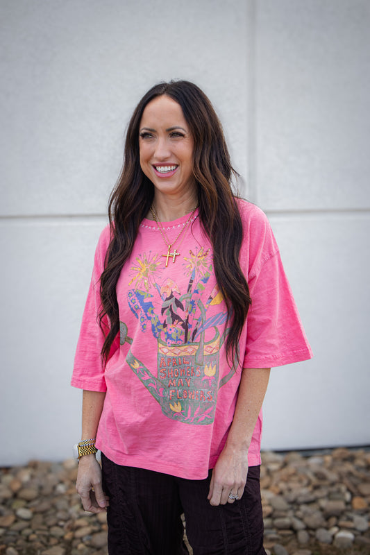 Woman wearing a pink t-shirt with a colorful graphic design against a white wall.