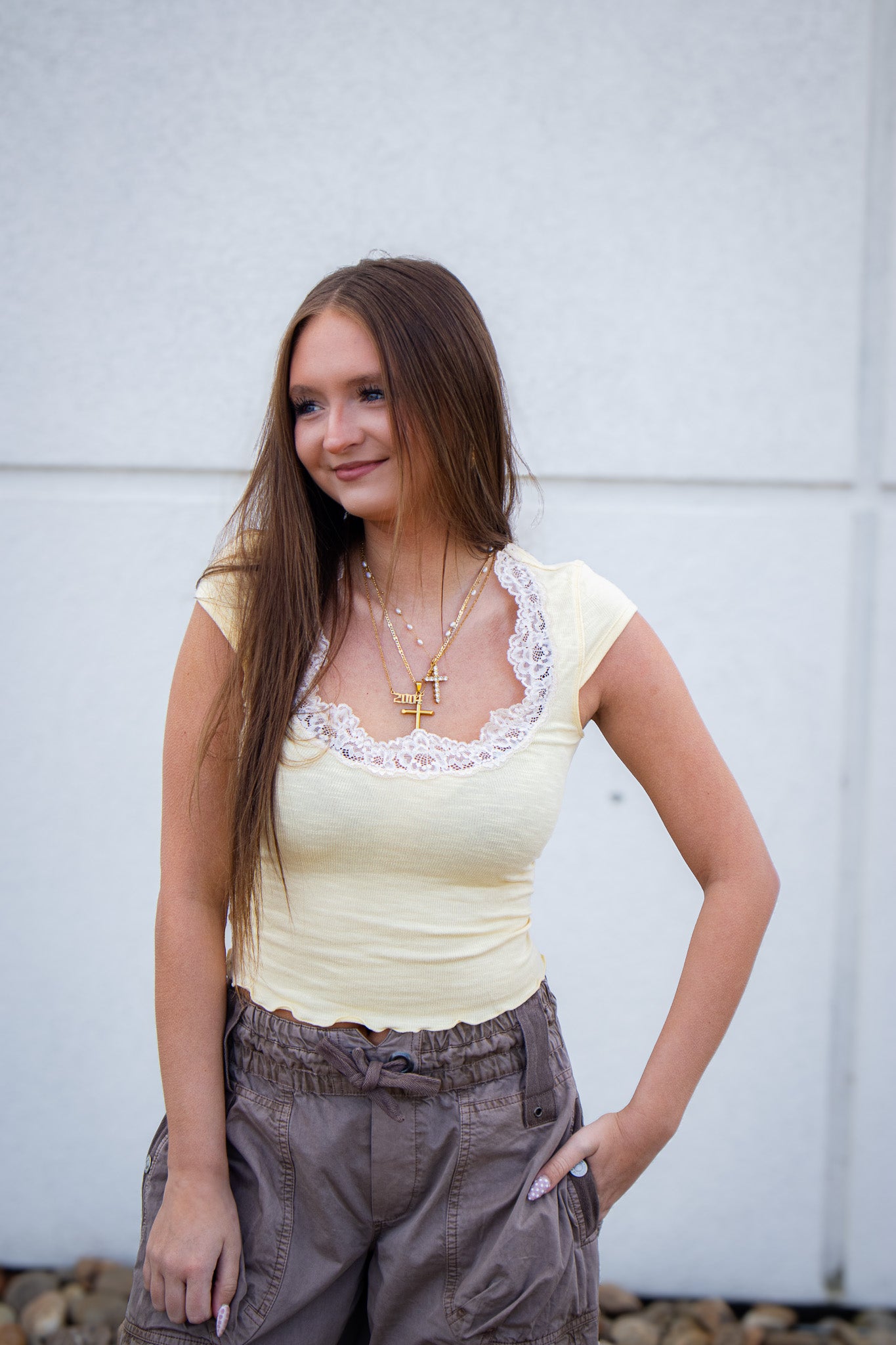 Woman wearing a yellow top with lace details and brown pants against a light gray background