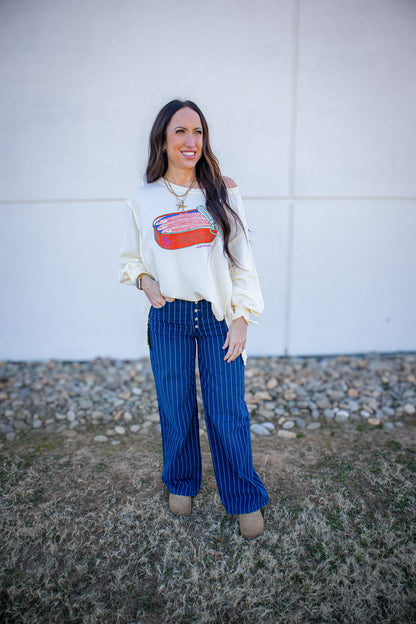 Woman wearing a white oversized sweatshirt with a sardines graphic design and blue striped pants standing in front of a white wall.