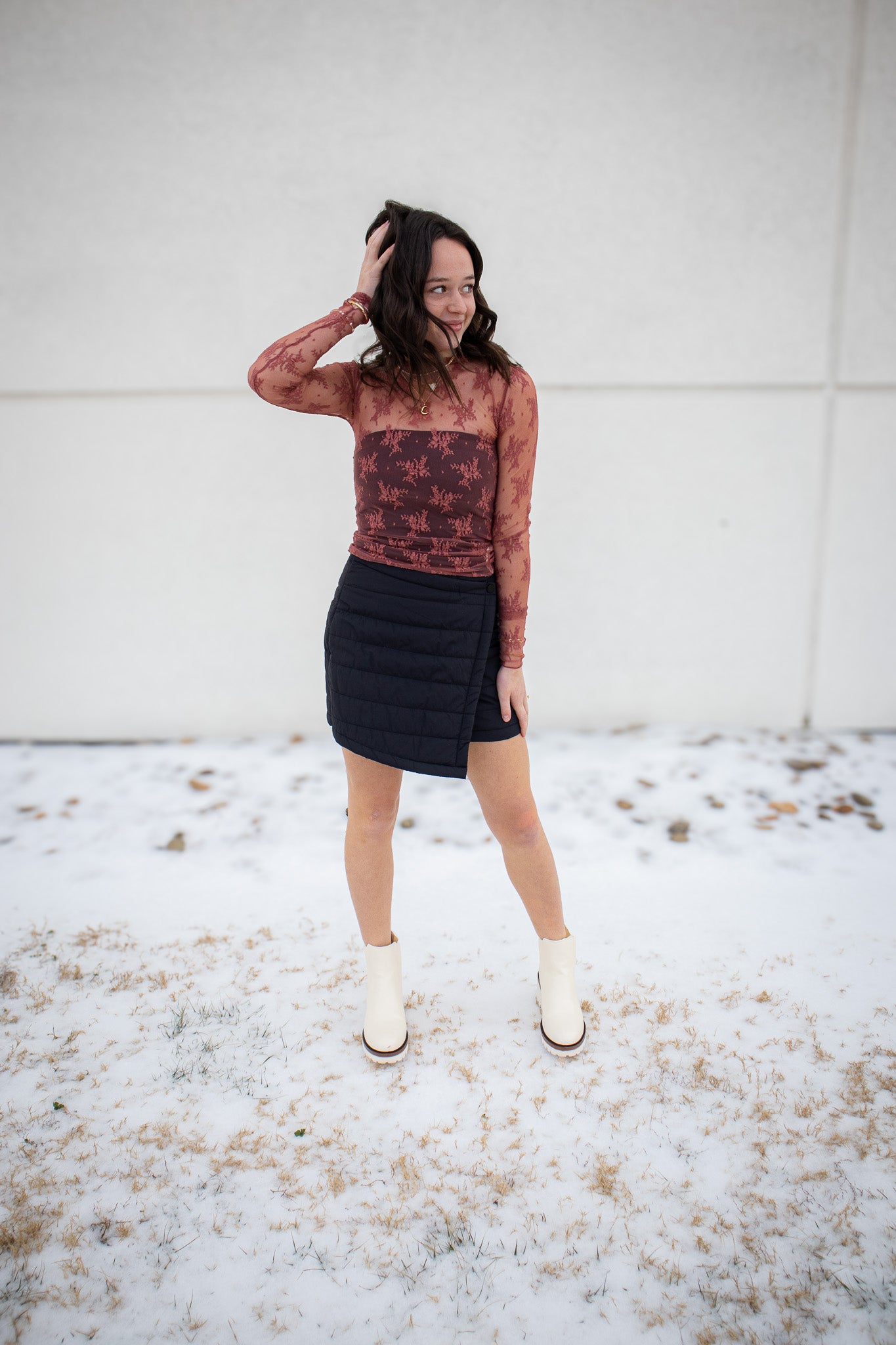 Woman standing outdoors on a snowy ground wearing a patterned top and black skirt.