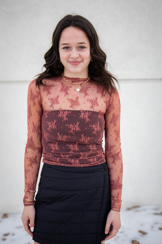 Woman wearing a red floral long-sleeve top and black skirt against a white wall.