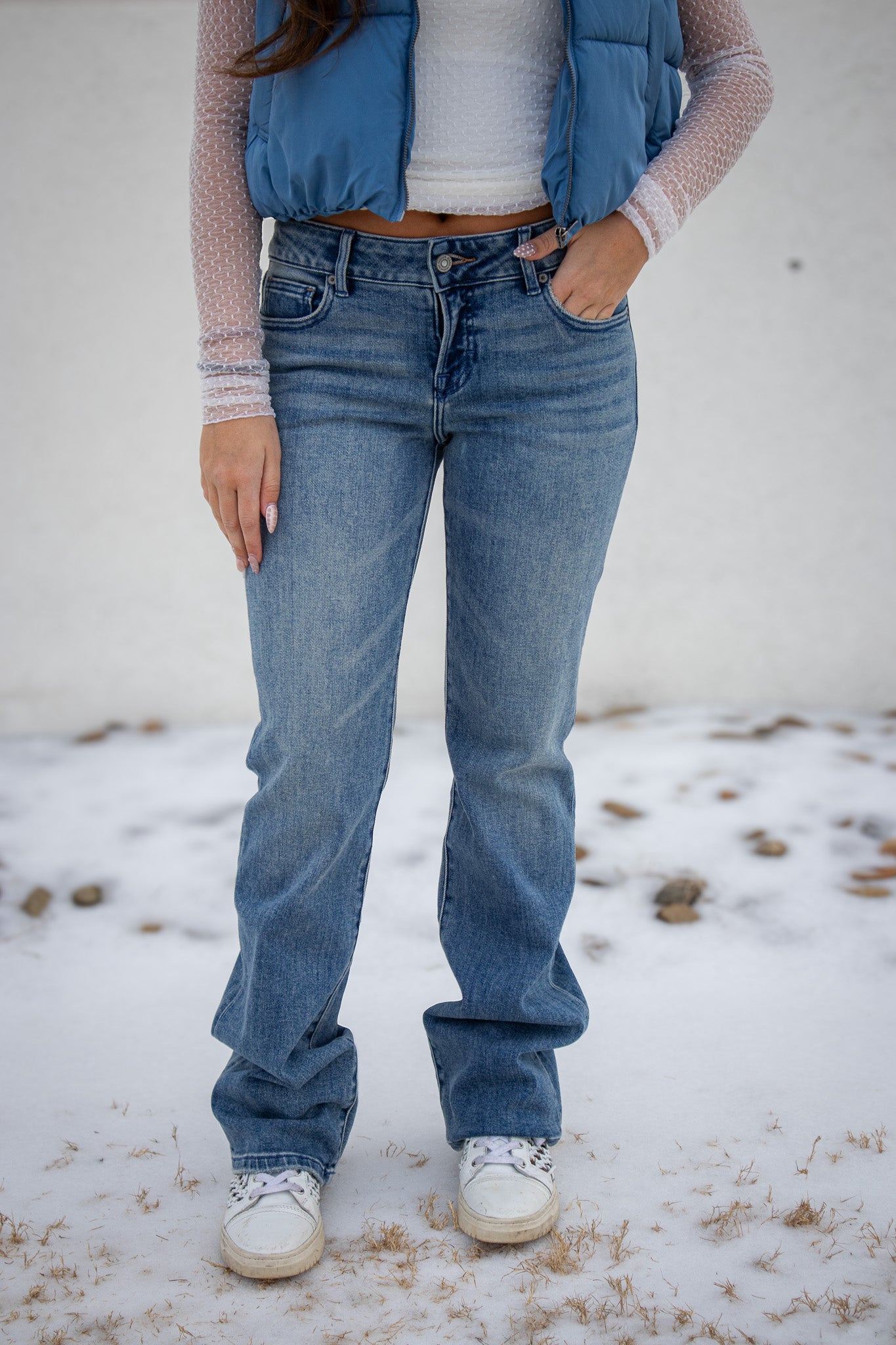 Person wearing blue jeans and a blue vest standing on a snowy ground.