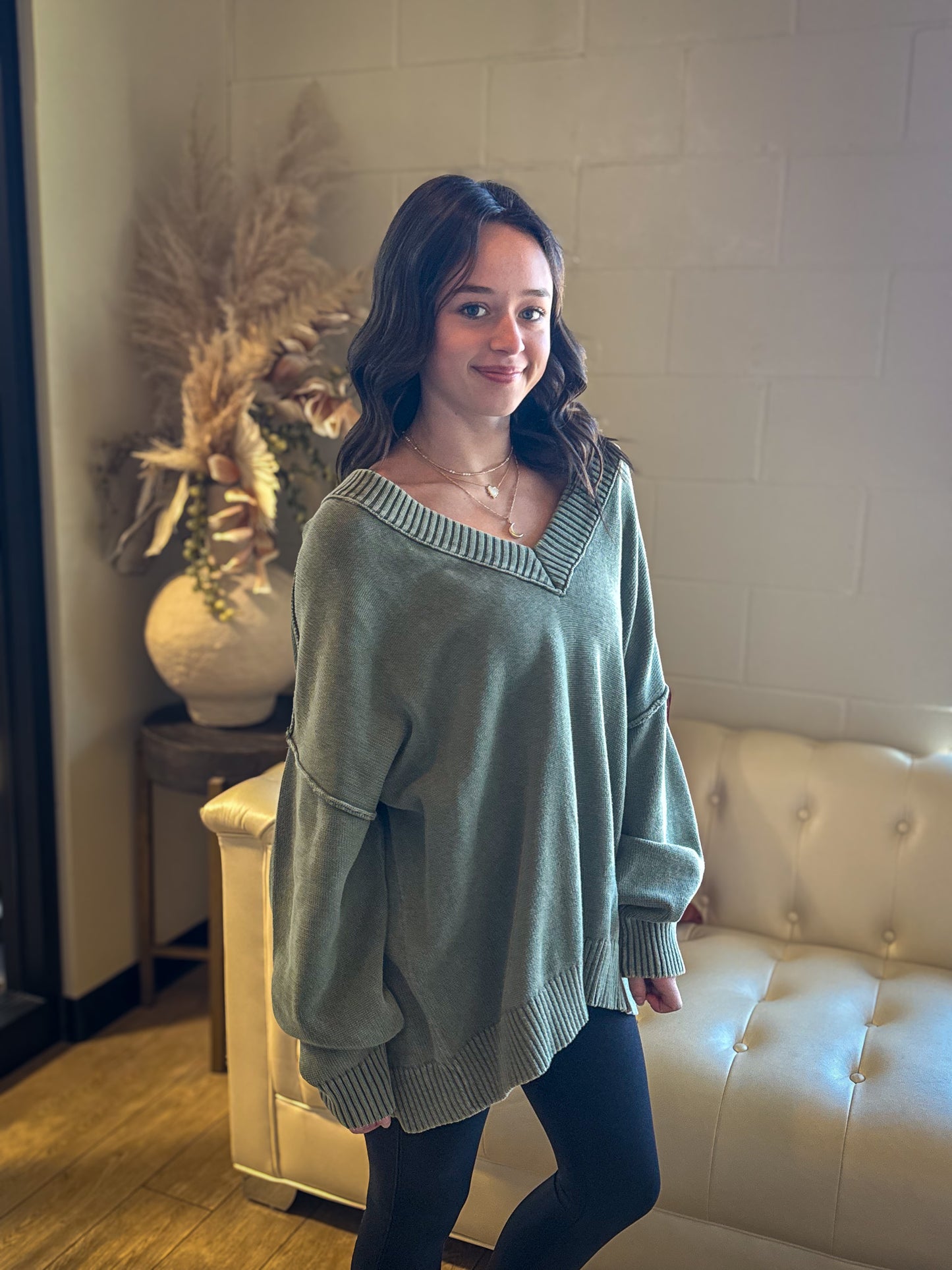 Woman wearing a green sweater standing in a room with a white couch and decorative plant.