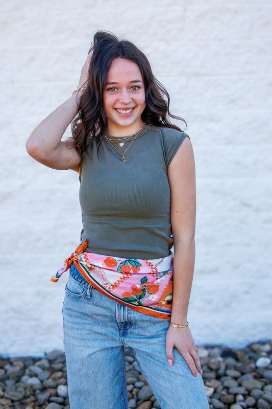 Woman wearing a fun printed silky scarf around her waist against a white wall.