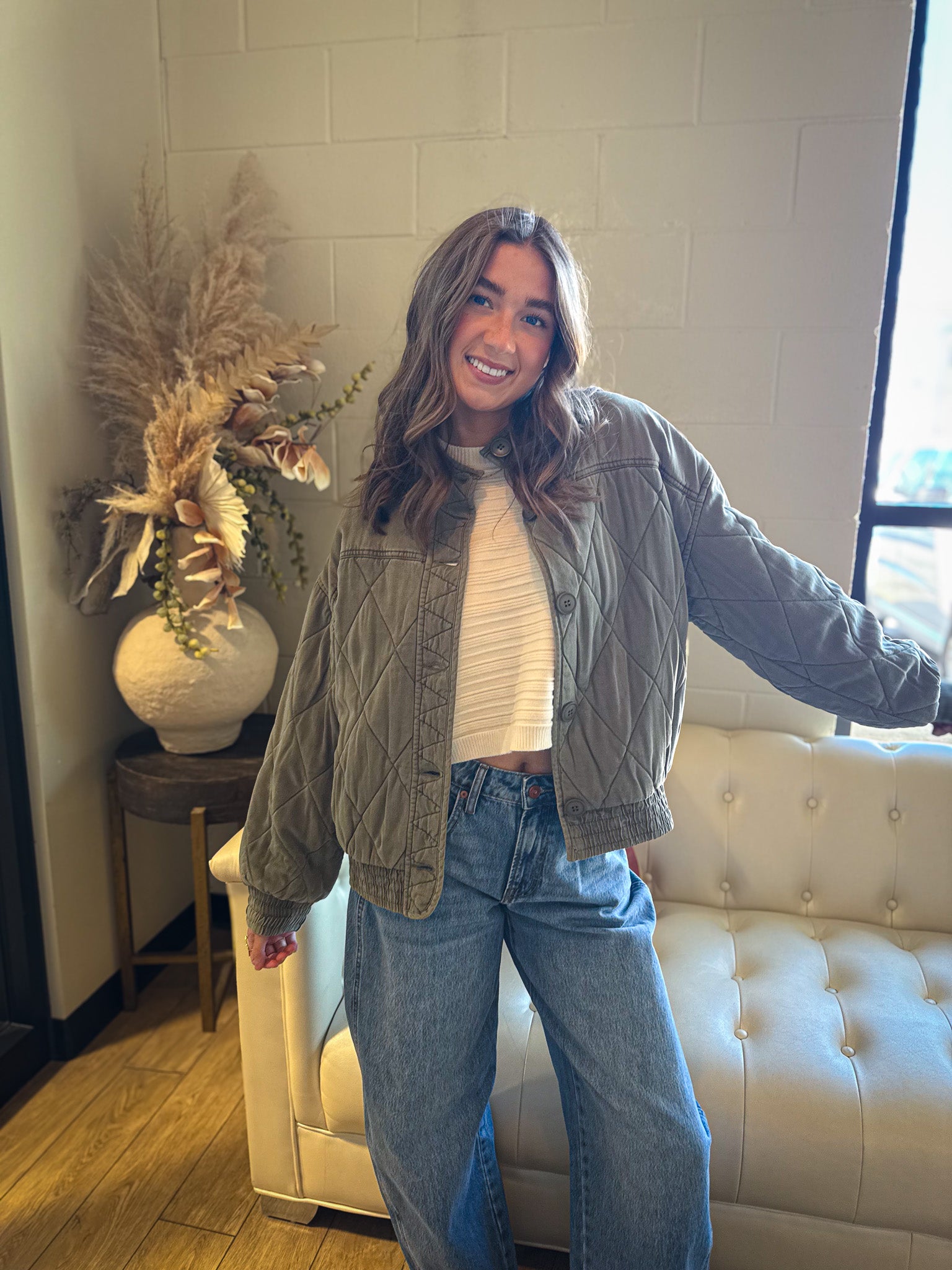 Woman standing in a room with a white couch and decorative plant.
