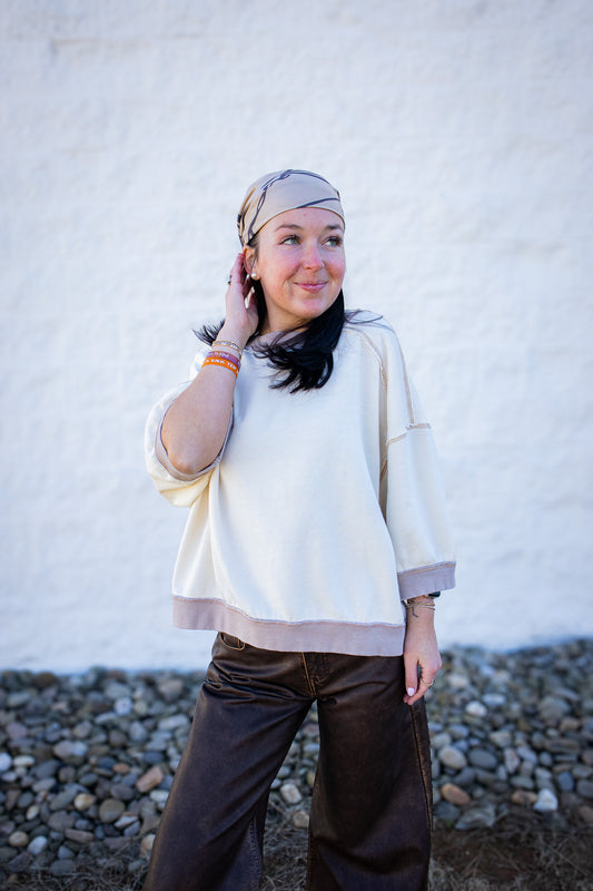 Woman wearing a white sweater and brown pants against a white wall.