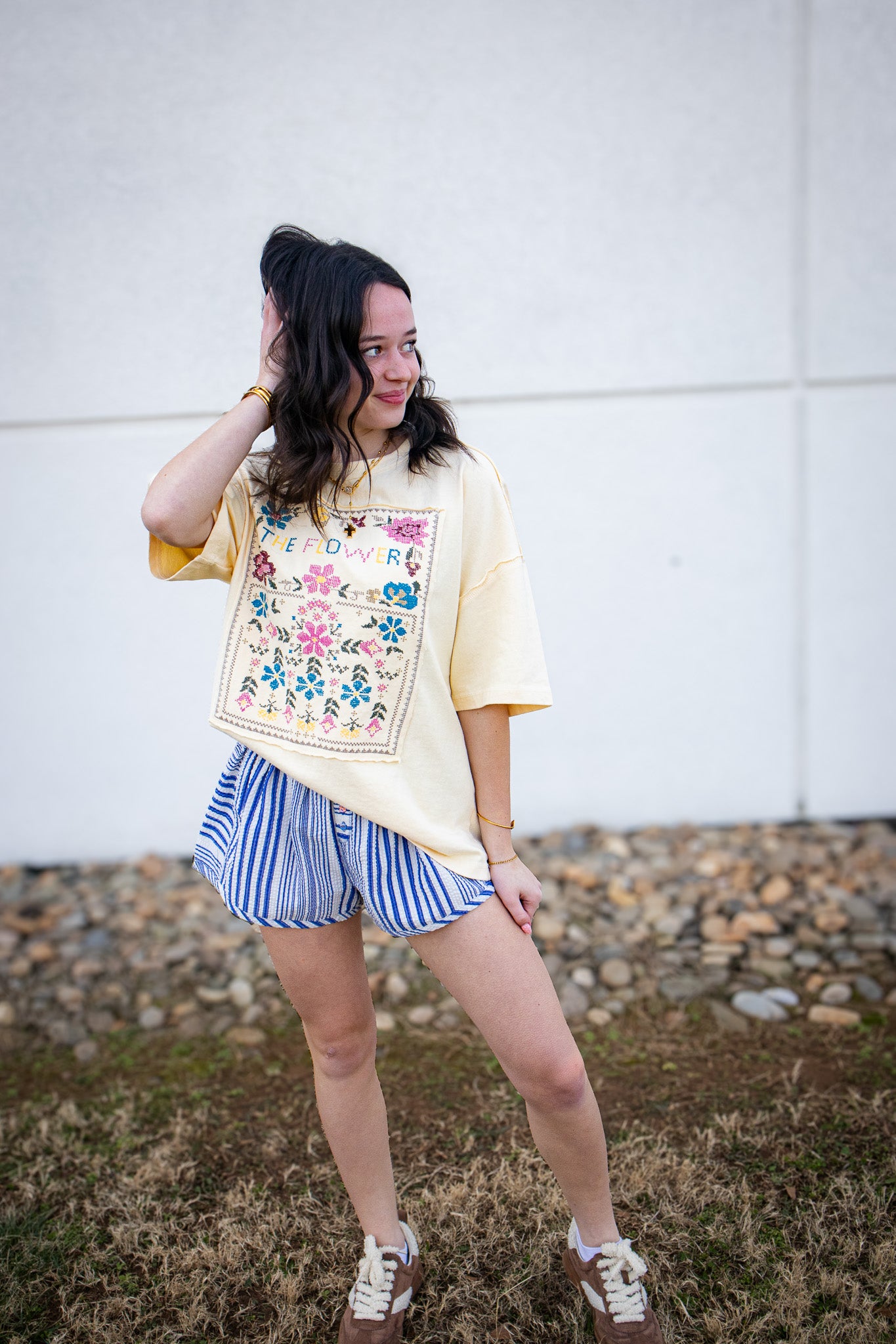 Woman wearing a floral embroidered shirt and striped shorts outdoors.