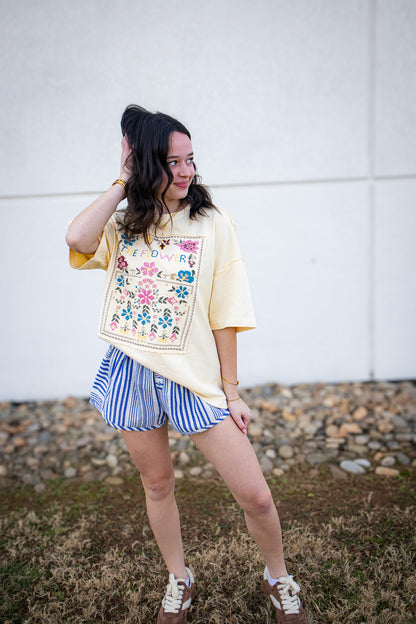 Woman wearing a floral embroidered shirt and striped shorts outdoors.