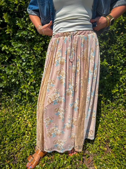 Person wearing a floral skirt and blue jacket standing in front of green foliage