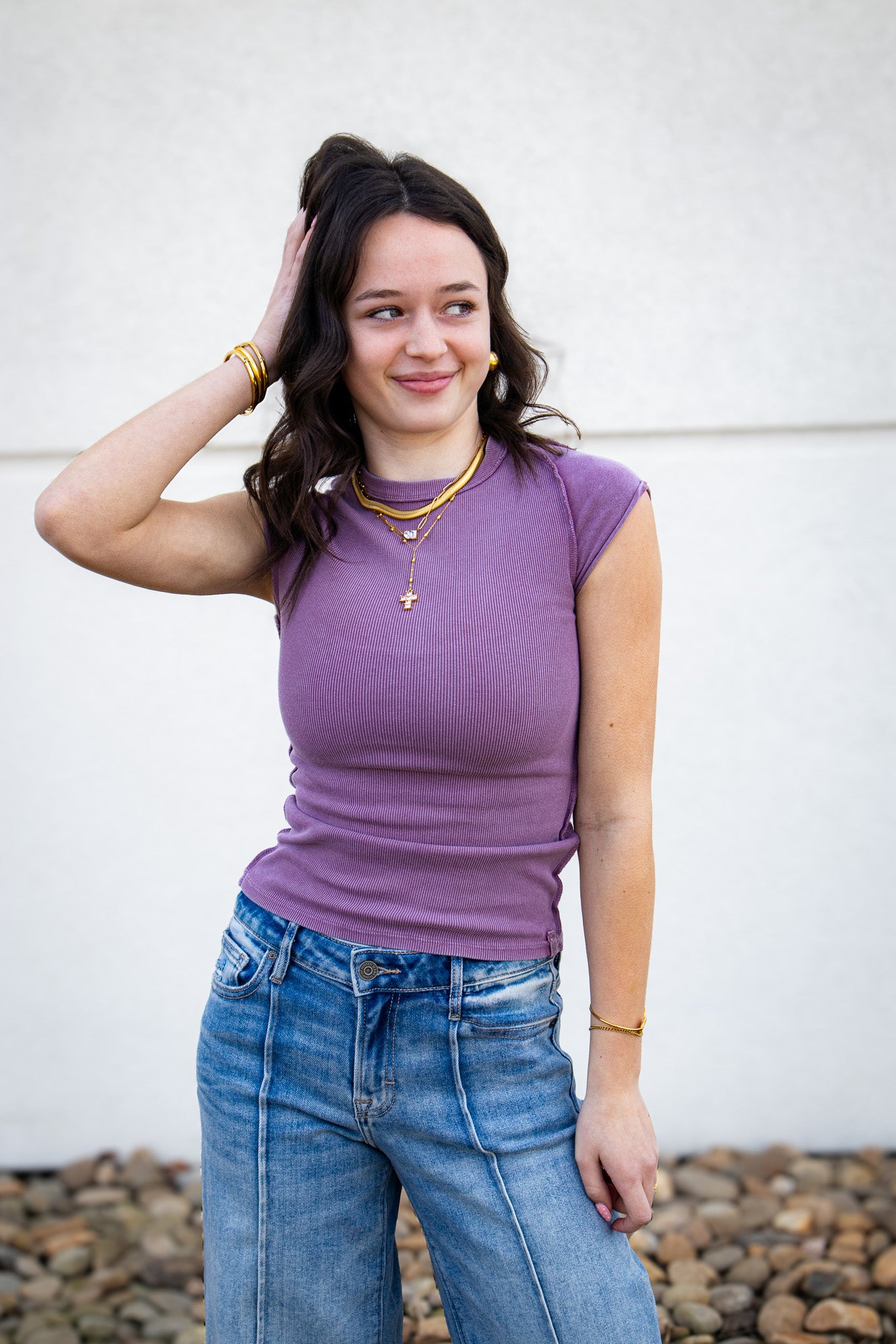 Woman wearing a purple top and blue jeans against a white wall.