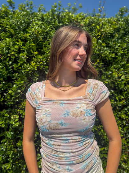Woman wearing a floral dress standing in front of green bushes