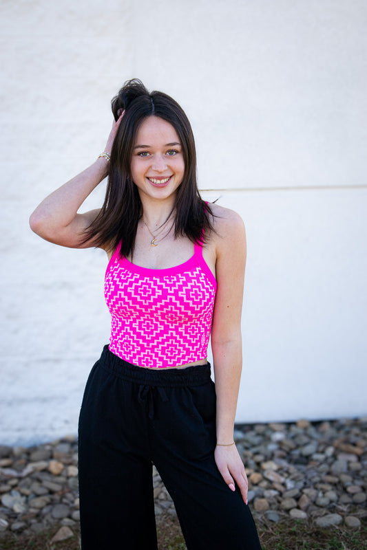 Woman wearing a bright pink tank top with a geometric pattern against a white wall.