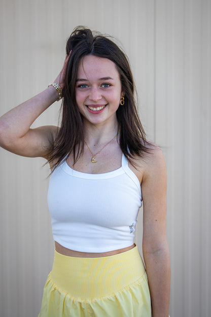 Woman wearing a white tank top and yellow athletic shorts against a plain background