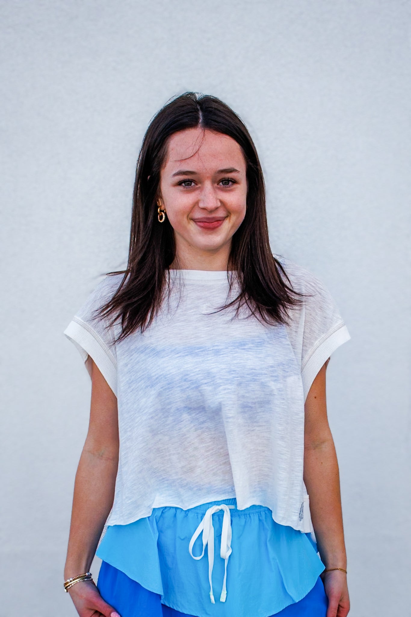 Woman wearing a light-colored top and blue shorts against a plain background