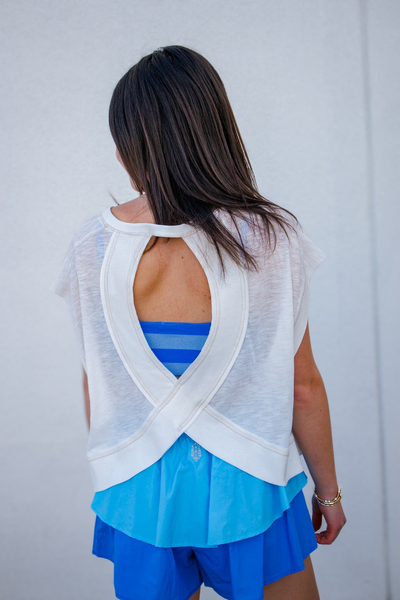 Woman wearing a white mesh top over a blue outfit against a light gray background