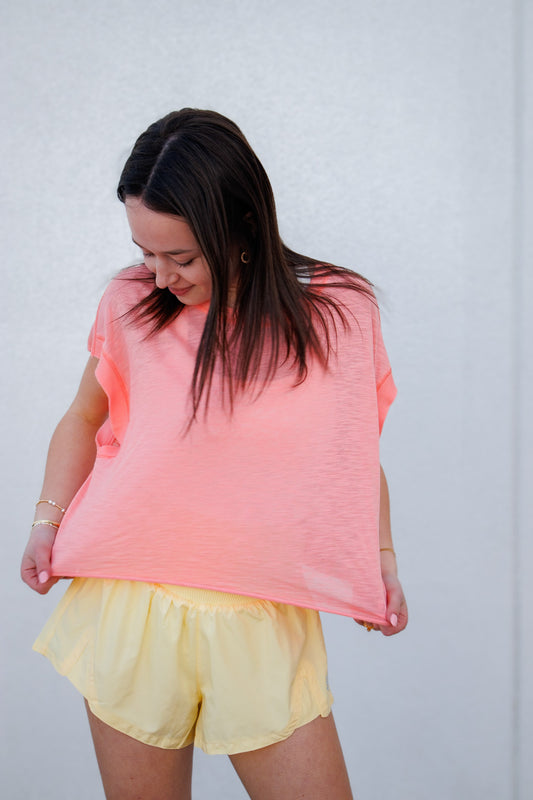 Woman wearing a pink sleeveless top and yellow shorts against a white background