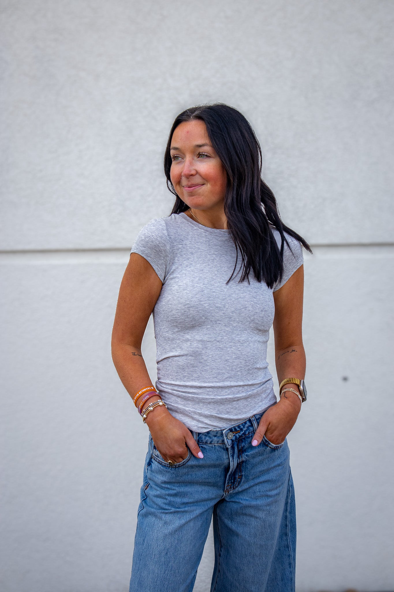 Woman wearing a gray t-shirt and blue jeans against a white wall