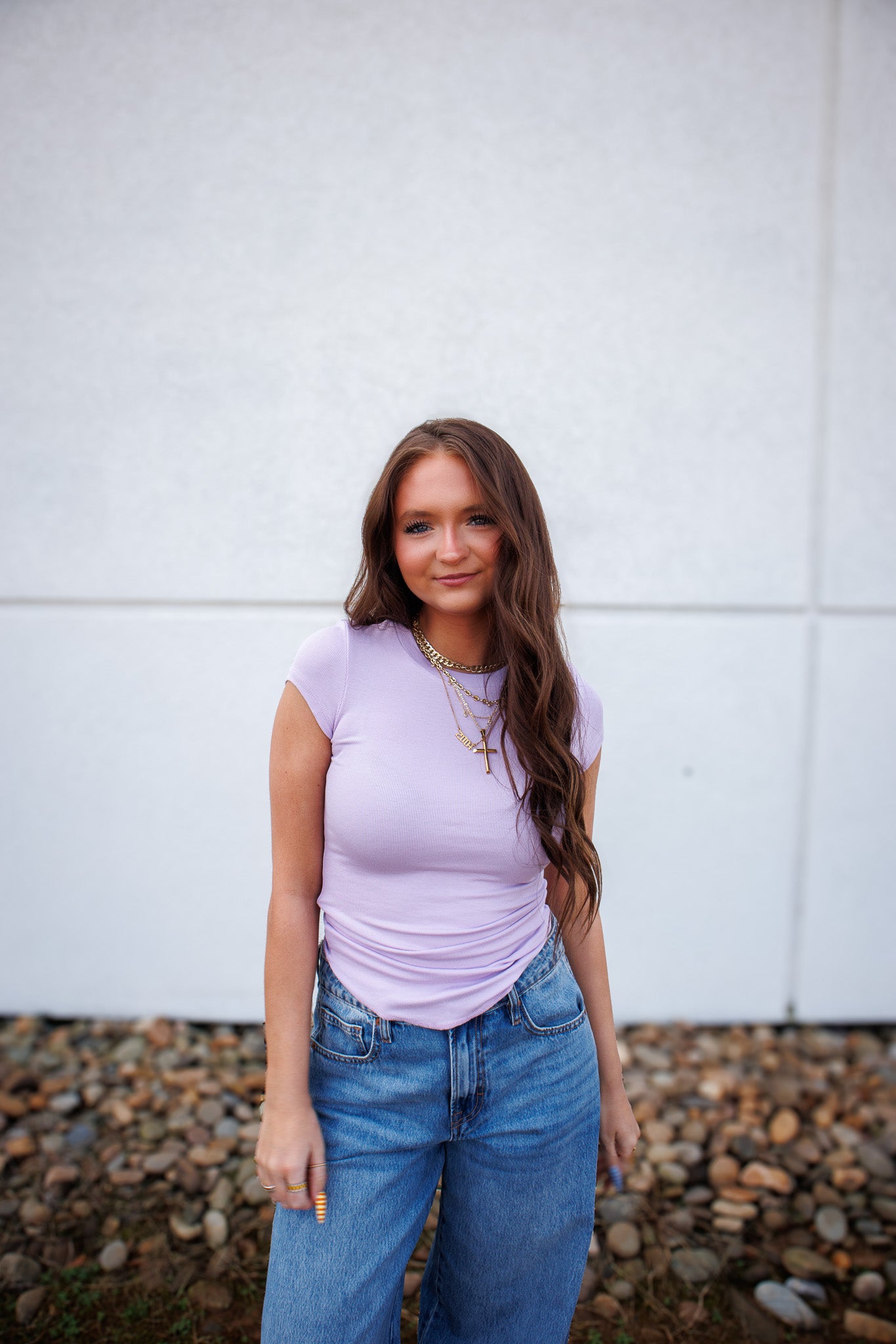 Girl in purple shirt and denim jeans against a white wall