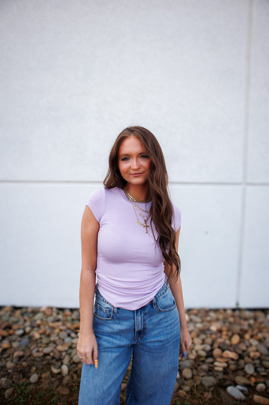Girl in purple shirt and denim jeans against a white wall
