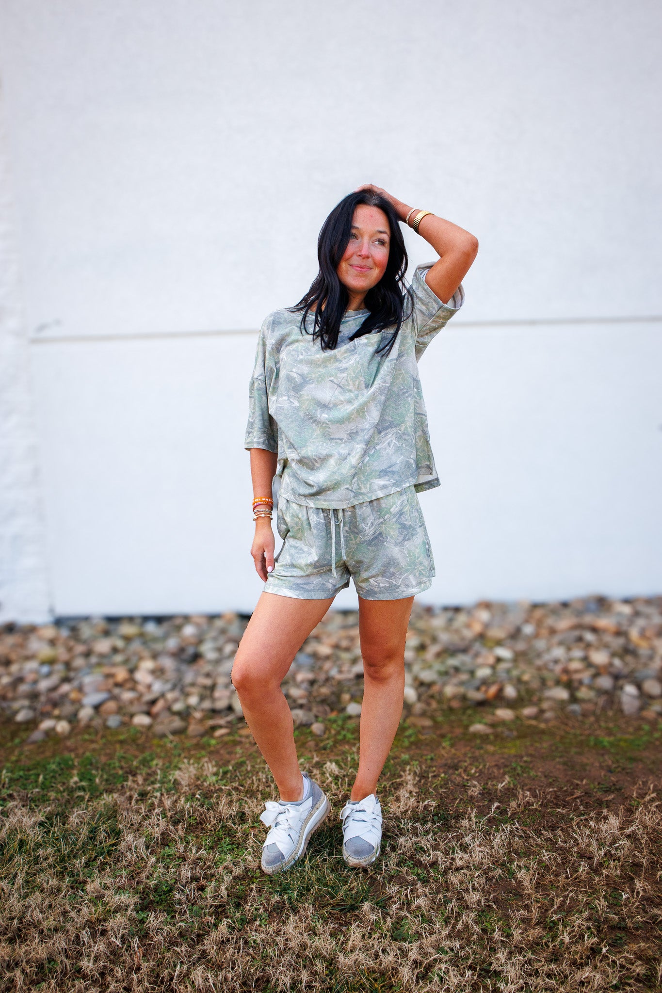 Girl in camo tee and shorts set and bow sneakers against white wall