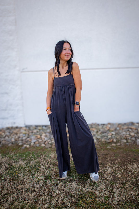 Woman wearing a dark blue jumpsuit standing against a white brick wall.