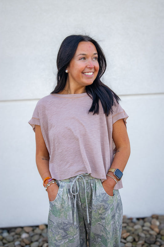 Woman wearing a beige t-shirt and patterned pants against a white wall.