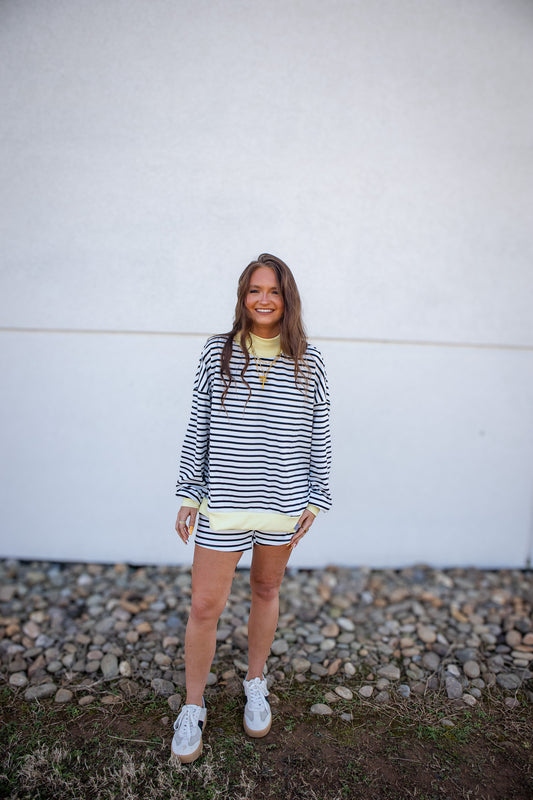 Woman wearing a striped outfit standing against a white wall with a textured ground.