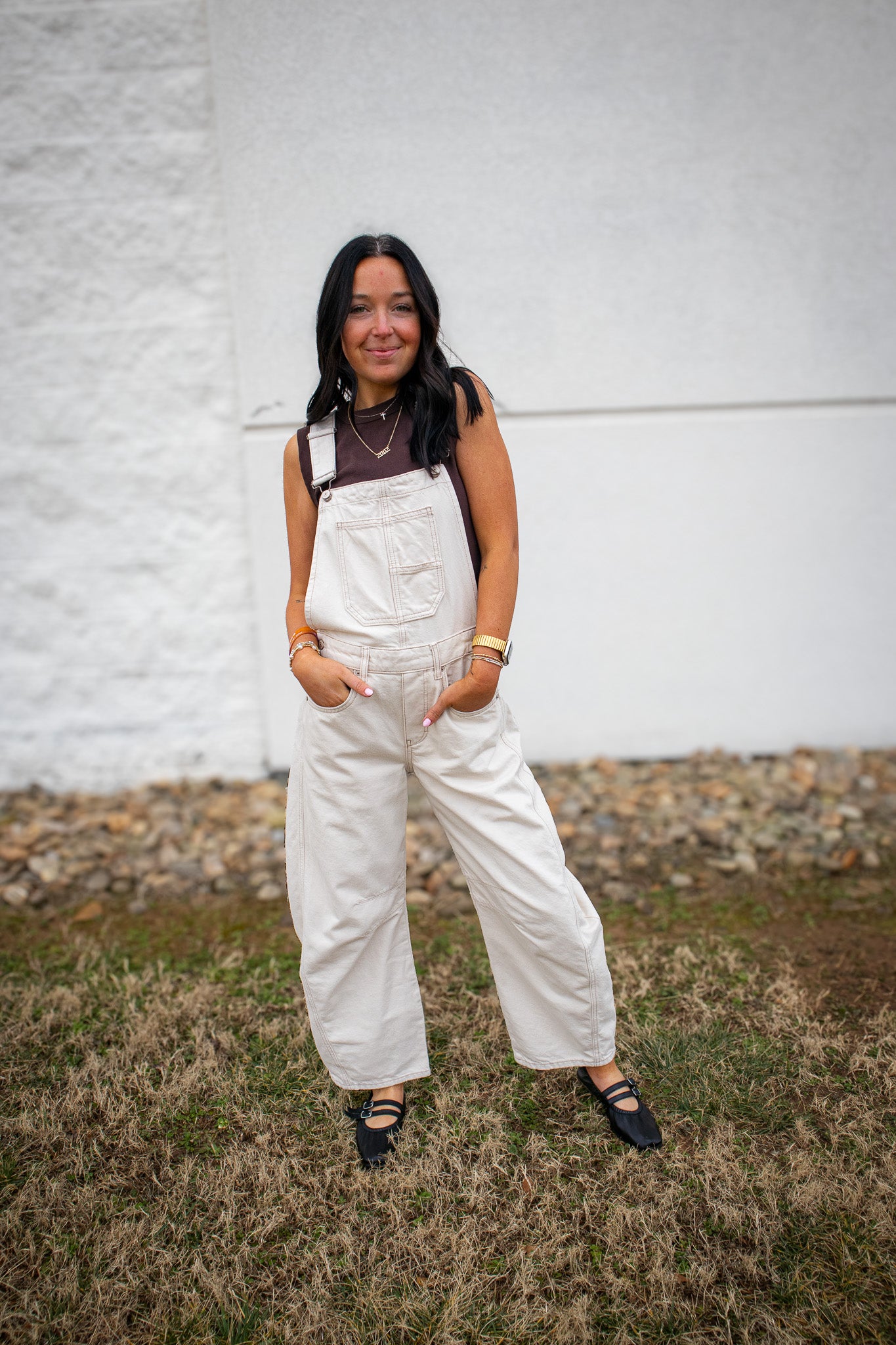 Woman wearing beige wide leg overalls styled with a brown sleeveless top and black flats, casual neutral outfit for everyday wear, standing outdoors