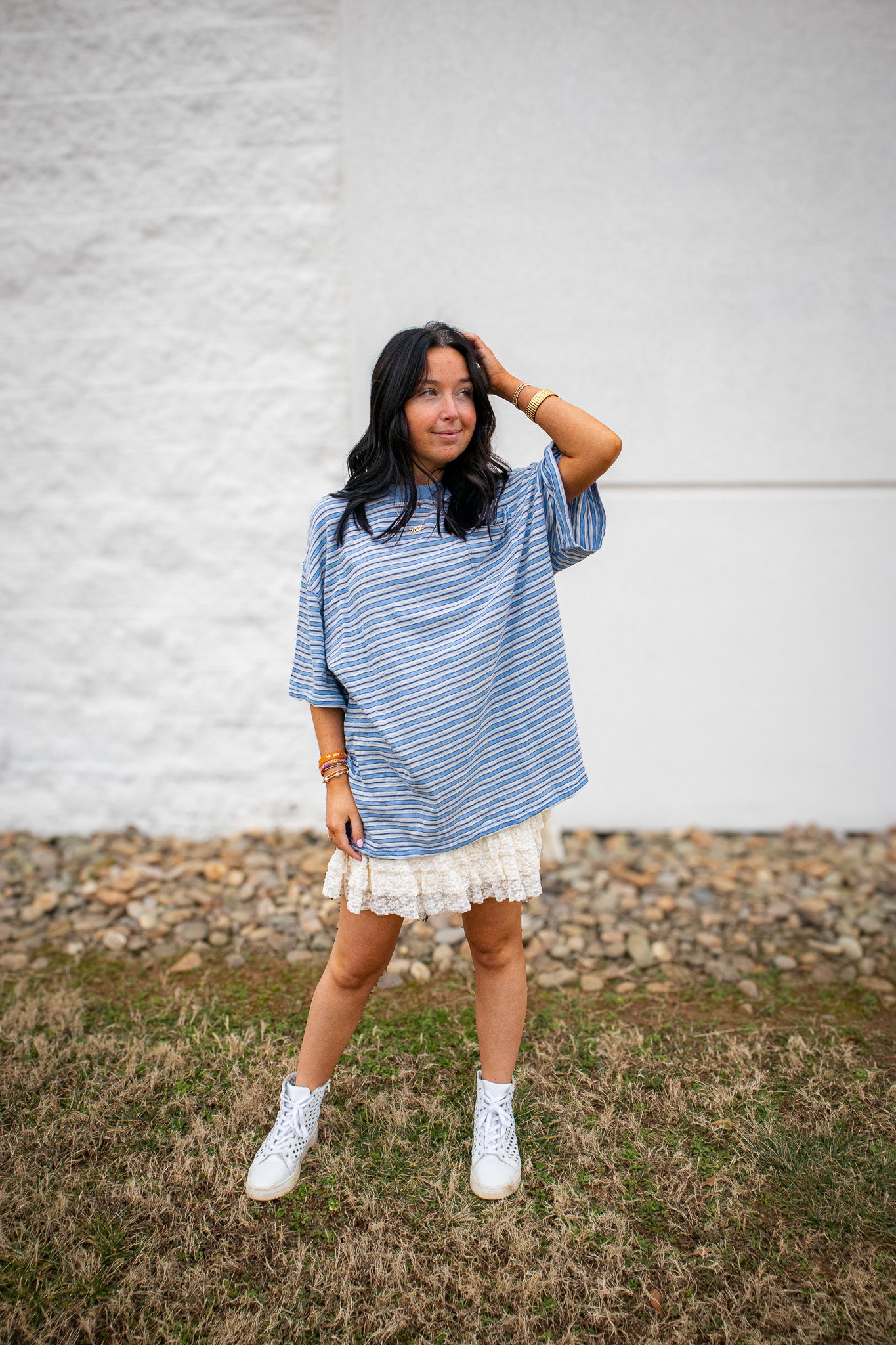 Woman wearing a blue striped tee over a white lace skort against a gray wall.