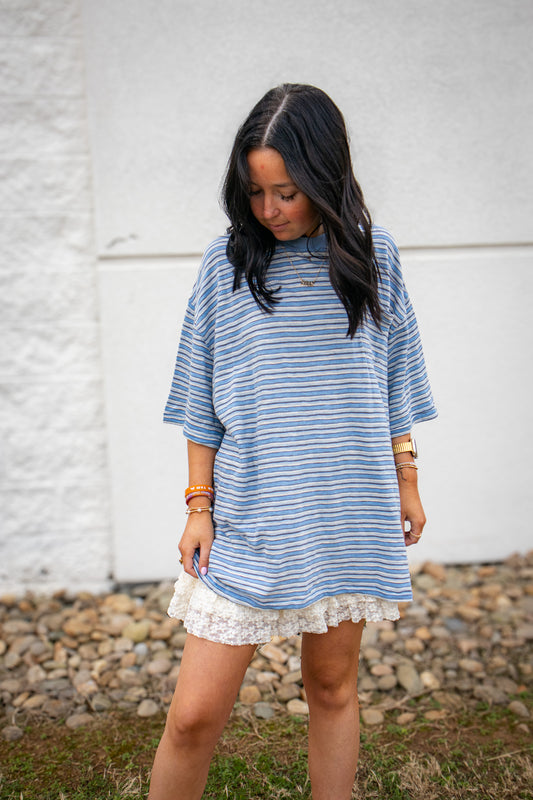 Woman wearing a blue and white striped tee with a white lace skort in front of a white wall.