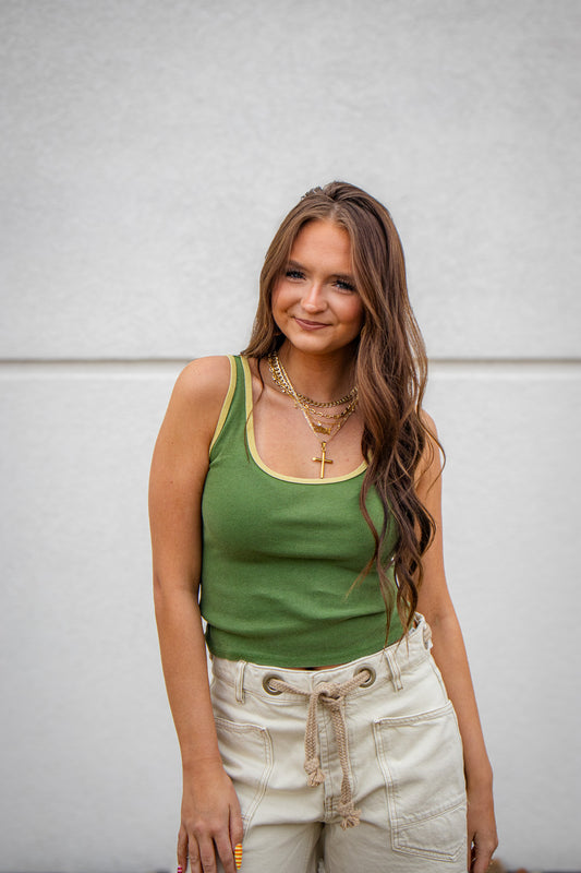 Woman wearing a green tank top and beige pants against a light gray background