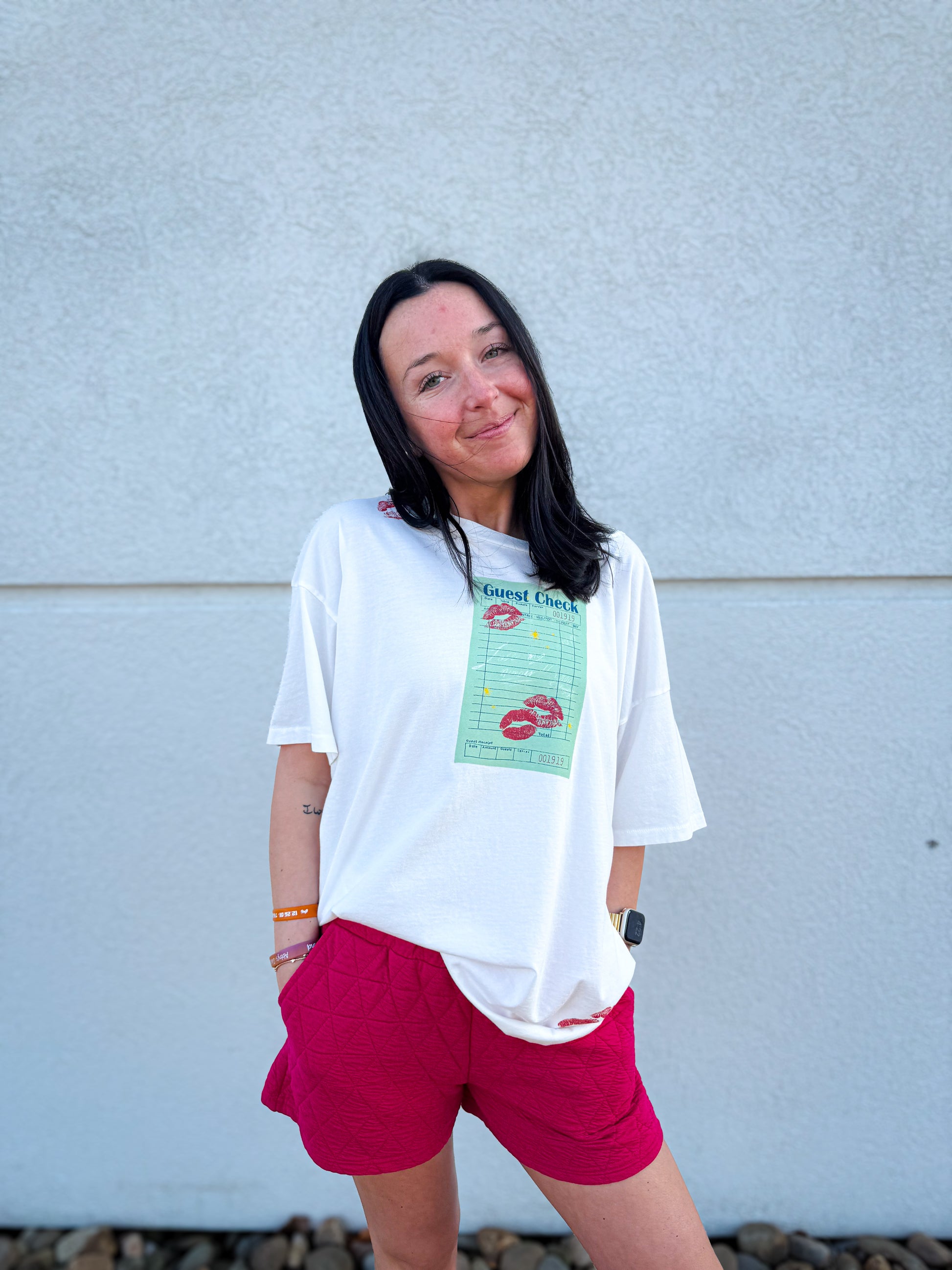Woman wearing a white t-shirt with a graphic design and pink shorts against a gray wall.
