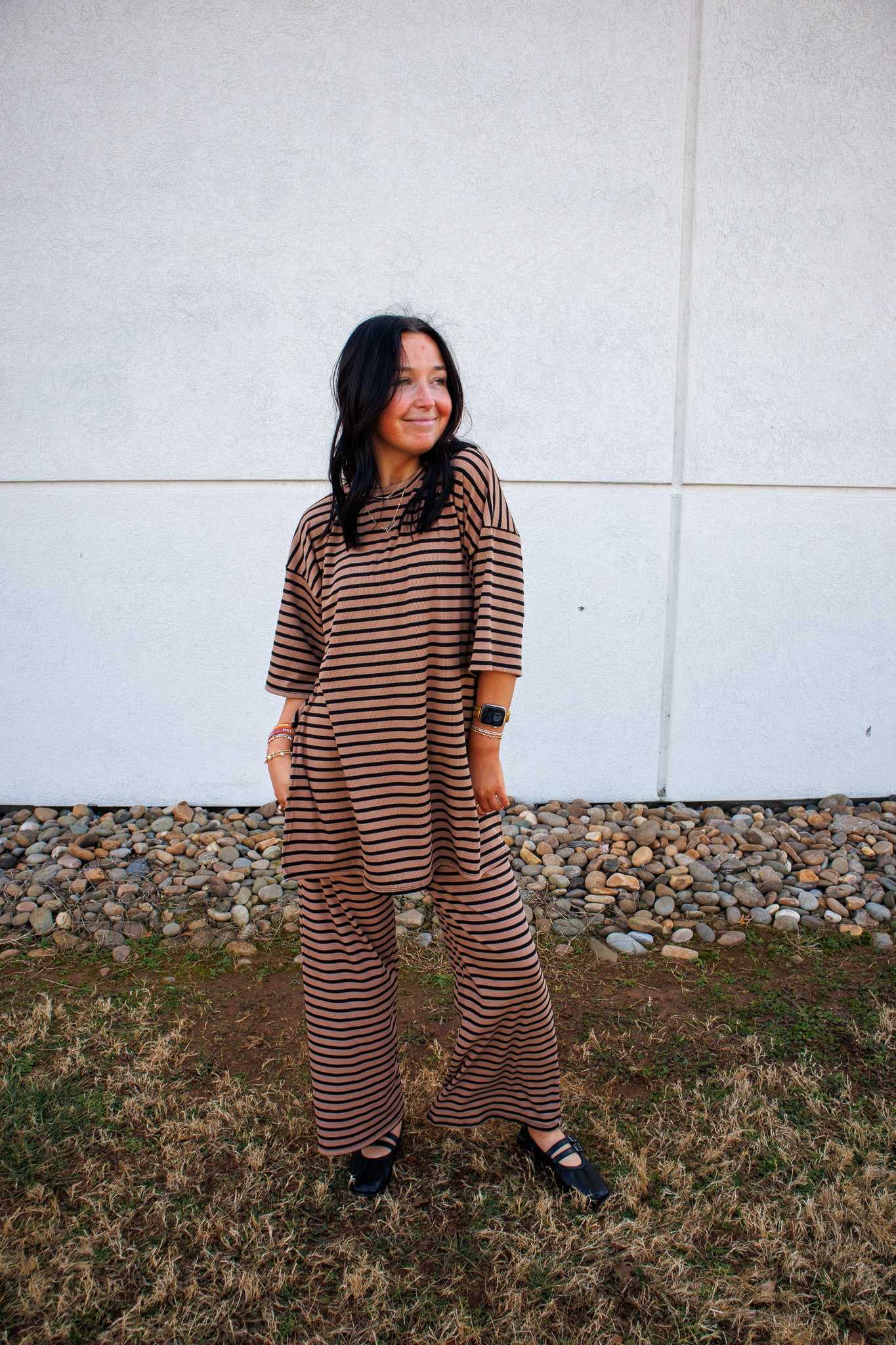 Woman wearing a brown and black striped set standing against a white wall.