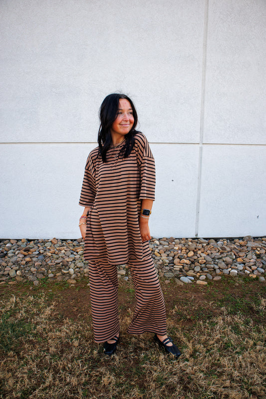 Woman wearing a brown and black striped set standing against a white wall.