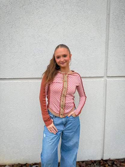 Woman wearing a pink and brown patterned top with blue wide-leg jeans against a white wall.