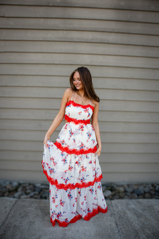 Woman wearing a floral dress with red trim standing against a beige wall.