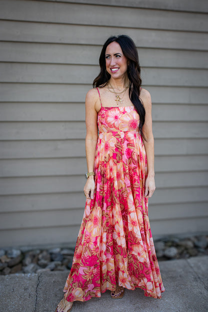 Woman wearing a floral dress standing against a neutral wall.