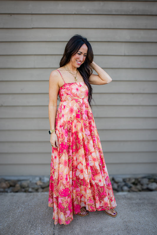 Woman wearing a floral dress standing against a plain wall.