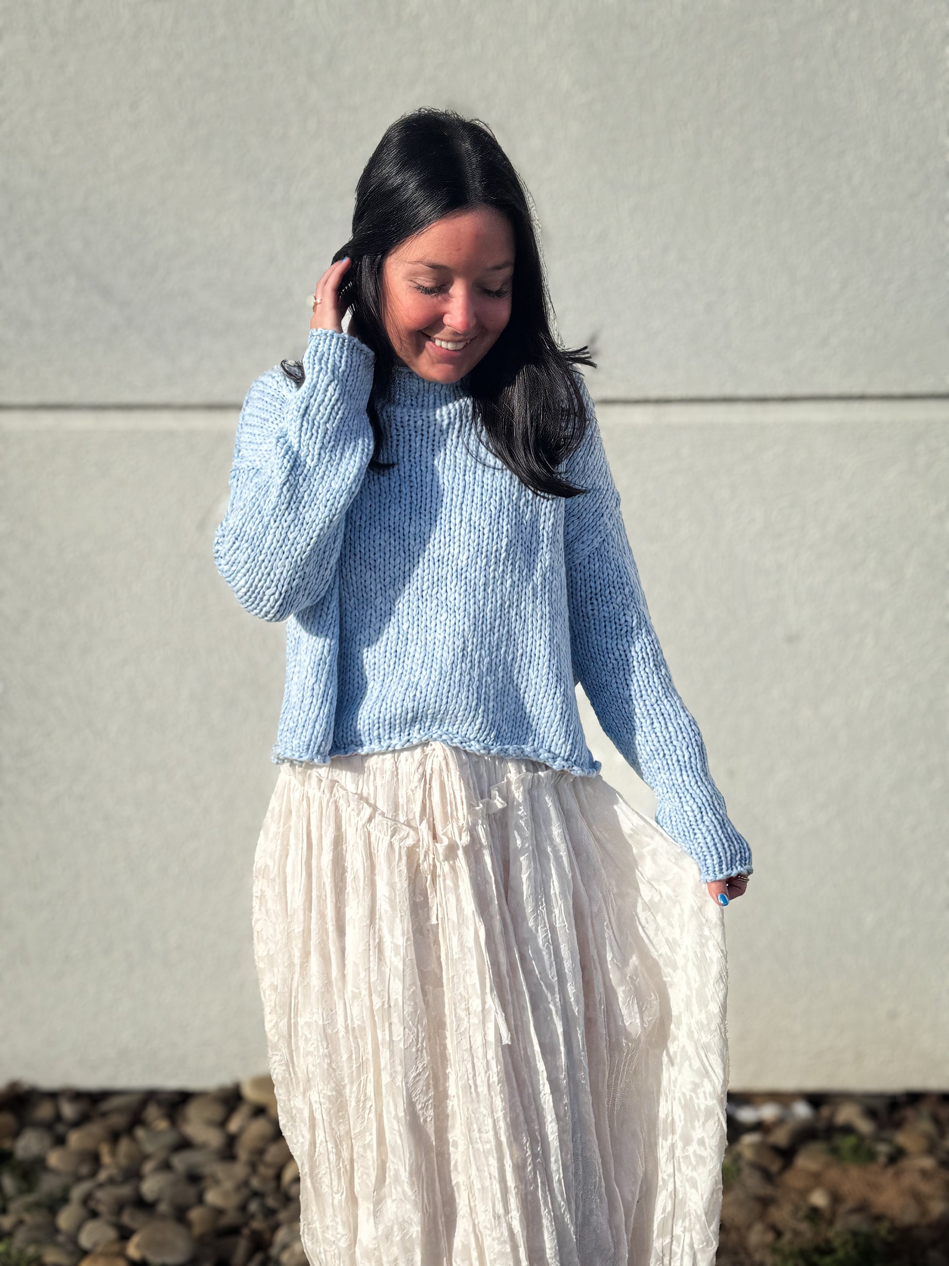 Woman wearing a light blue knitted sweater and a cream floral skirt against a plain background