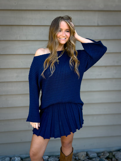 Woman wearing a blue sweater and skirt set against a neutral background