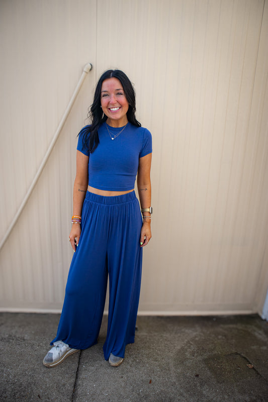 Woman wearing a blue outfit standing against a beige wall.