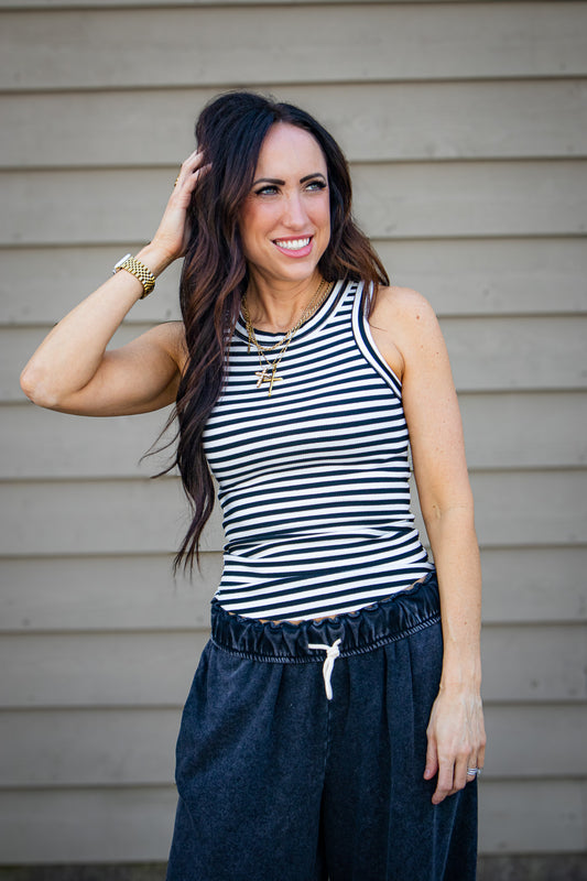 Woman wearing a striped tank top and black pants against a neutral background